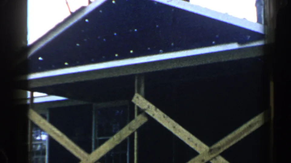 1957 Birmingham home-movie frame showing a dark roof edge, exposed diagonal lumber, and part of a window on a building.