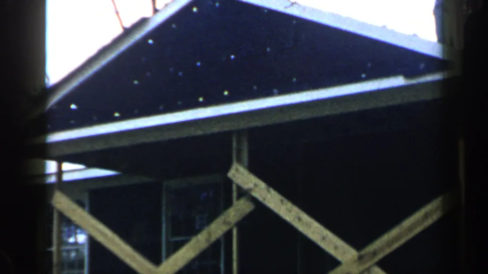 1957 Birmingham frame with diagonal support boards beneath a dark roof edge and a partially visible window.