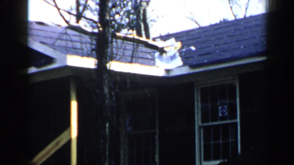 1957 Birmingham frame showing a dark facade, divided window, roof shingles, tree trunk, and exposed diagonal board.