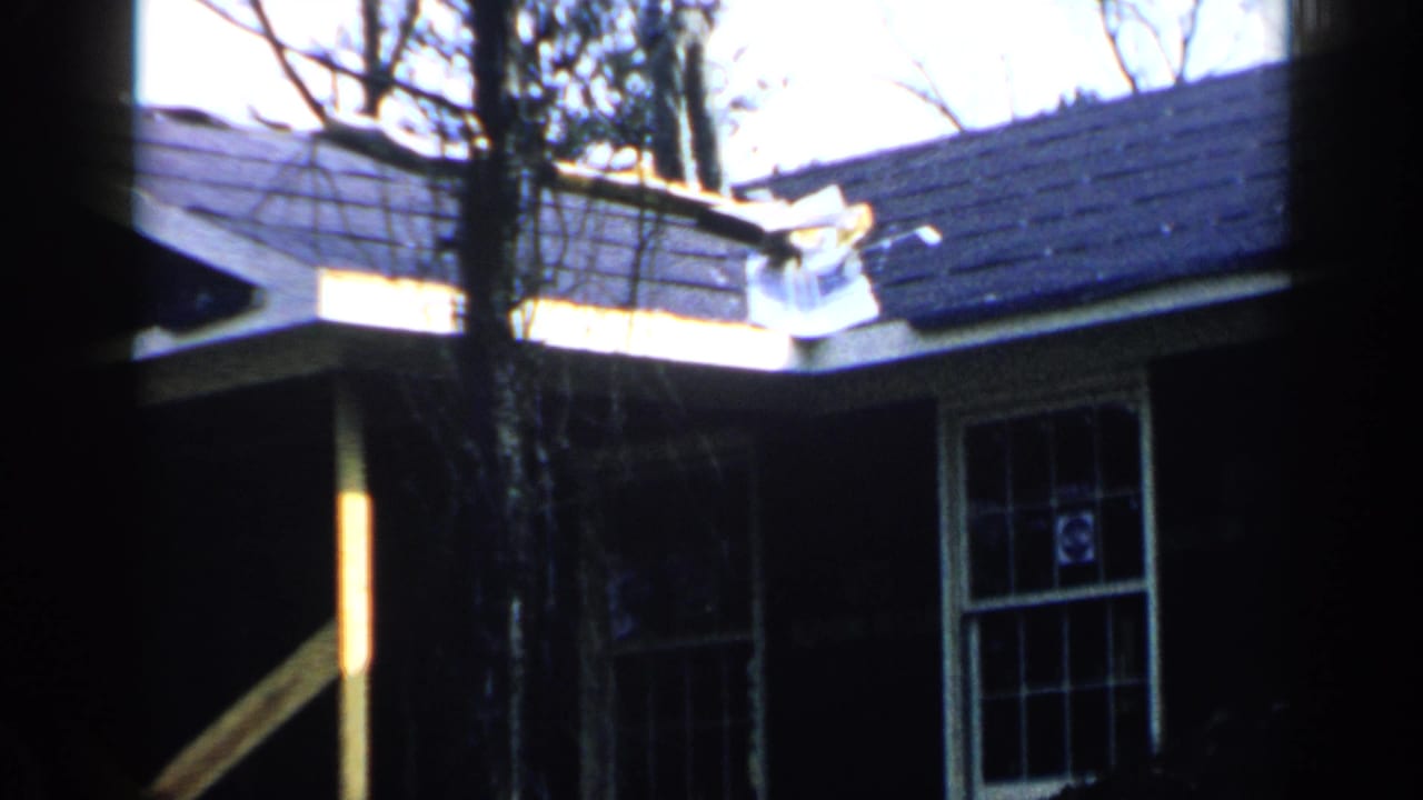 White wood house exterior with dark roof, divided window, and bare trees.
