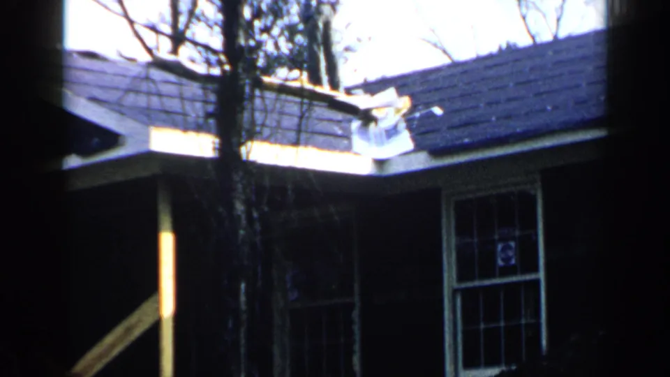 1957 Birmingham home-movie frame showing a white wood house, dark shingle roof, divided window, and bare trees in front.