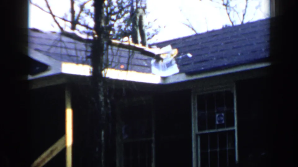 1957 Birmingham frame with a dark roof, light siding, divided window, bare trees, and a small white object near the roofline.