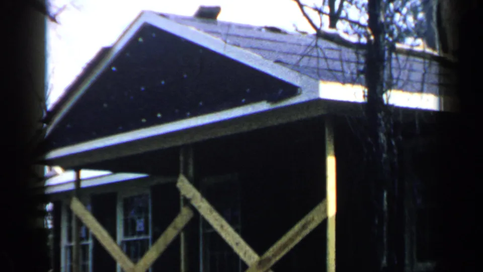 1957 Birmingham frame showing the gable end of a wood house with porch supports, divided windows, dark shingles, and bare trees.