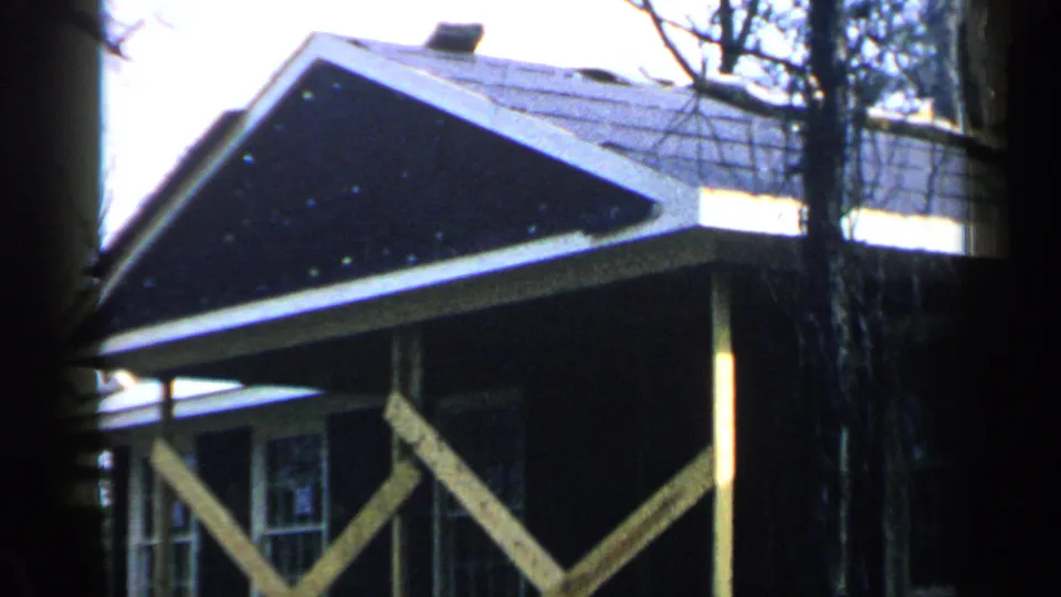 1957 Birmingham home-movie frame of a wood house gable, porch supports, windows, dark roof, and bare trees in winter light.