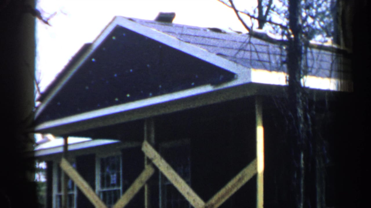 Dark-sided house with porch supports and gabled roof among trees.