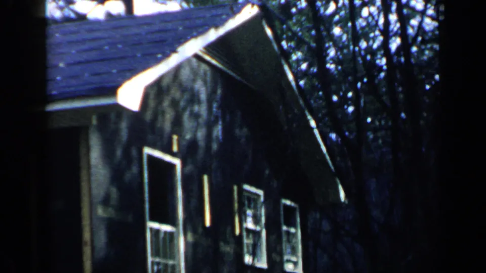1957 Birmingham-area frame focused on the side wall of a dark residential building with white-trimmed windows and trees.