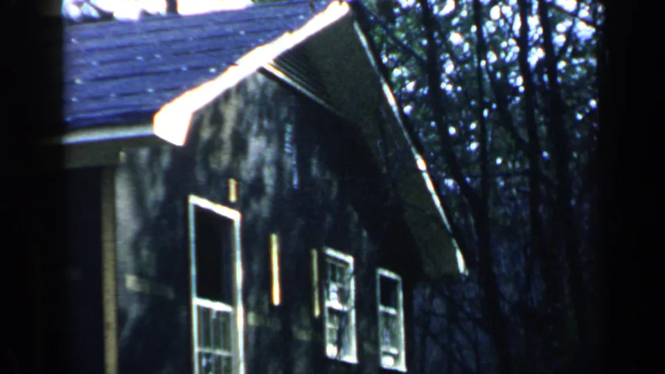 1957 Birmingham-area 8mm view of the dark house side, showing a tall framed opening, smaller windows, roofline, and trees.