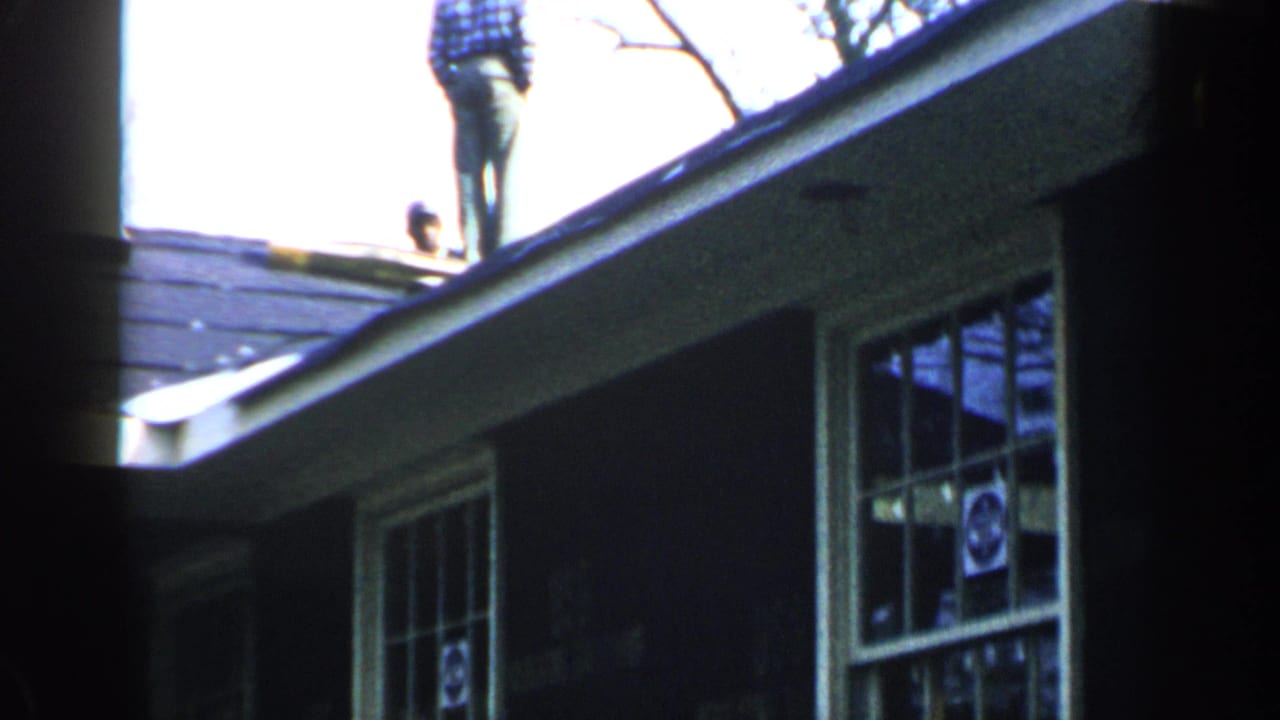 Two men partly visible near a shingled residential roof and upper windows.
