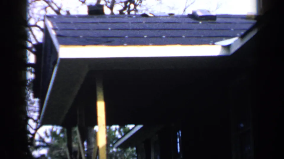 1957 Birmingham 8mm view of a house exterior from below, showing roof shingles, eaves, porch post, and surrounding branches.