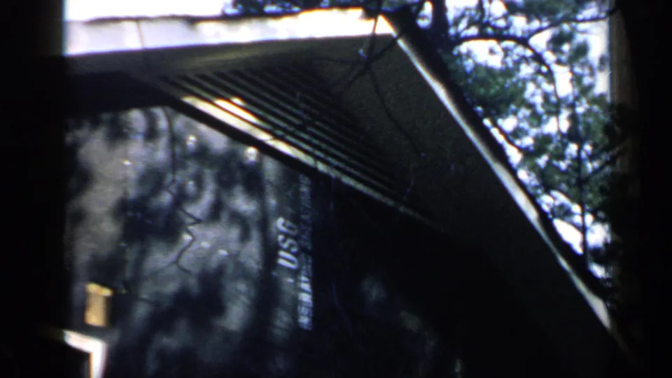 1957 Birmingham 8mm frame showing angled eaves, a textured wall or panel, reflected branches, and faint unreadable lettering.