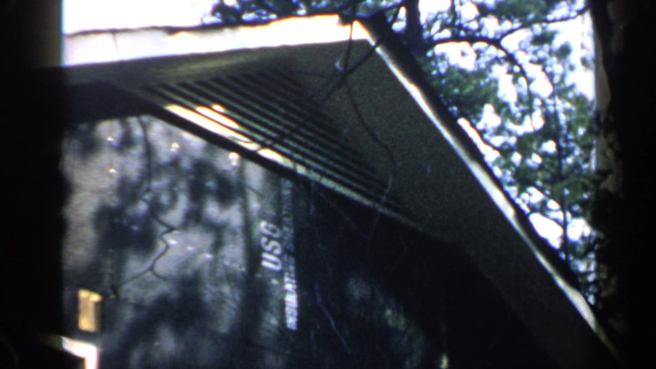 Dark house exterior with overhanging eaves, trees, and a vertical USC marking.