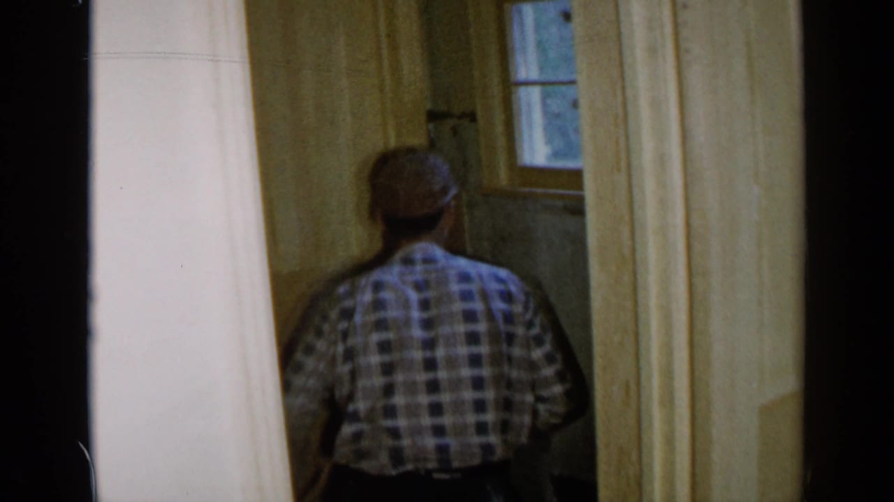 Man seen from behind working near a small window in an unfinished room.