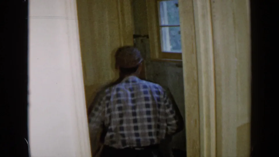 A man viewed from behind works inside a Birmingham, Alabama interior, with exposed wall surfaces and a small window visible.