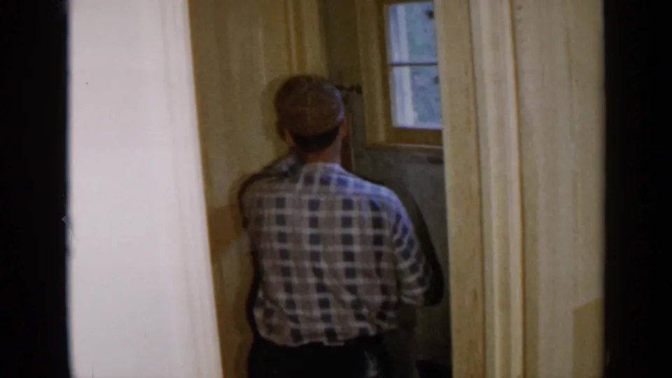 The home-movie frame shows the man continuing wall work in an unfinished private room in Birmingham in 1957.