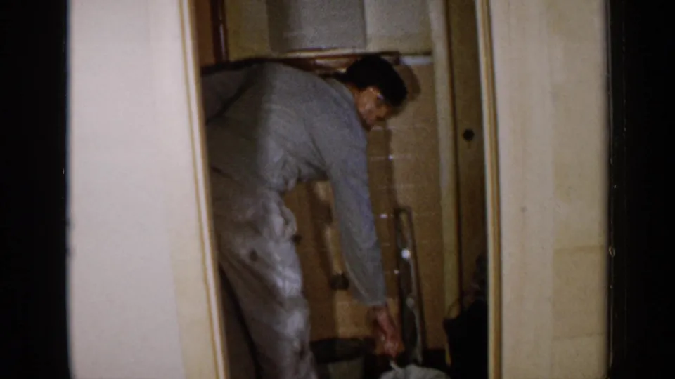 A man bends down with tools near the floor of an unfinished Birmingham interior, with wall surfaces and doorway trim visible.