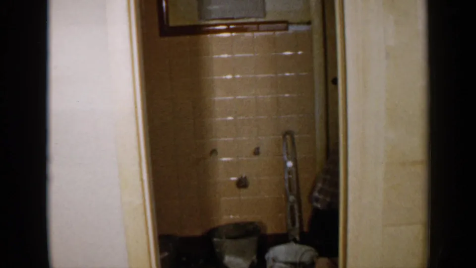 The final frame holds on the empty 1957 Birmingham bathroom, showing beige tile, exposed plumbing, a ladder, and supplies.