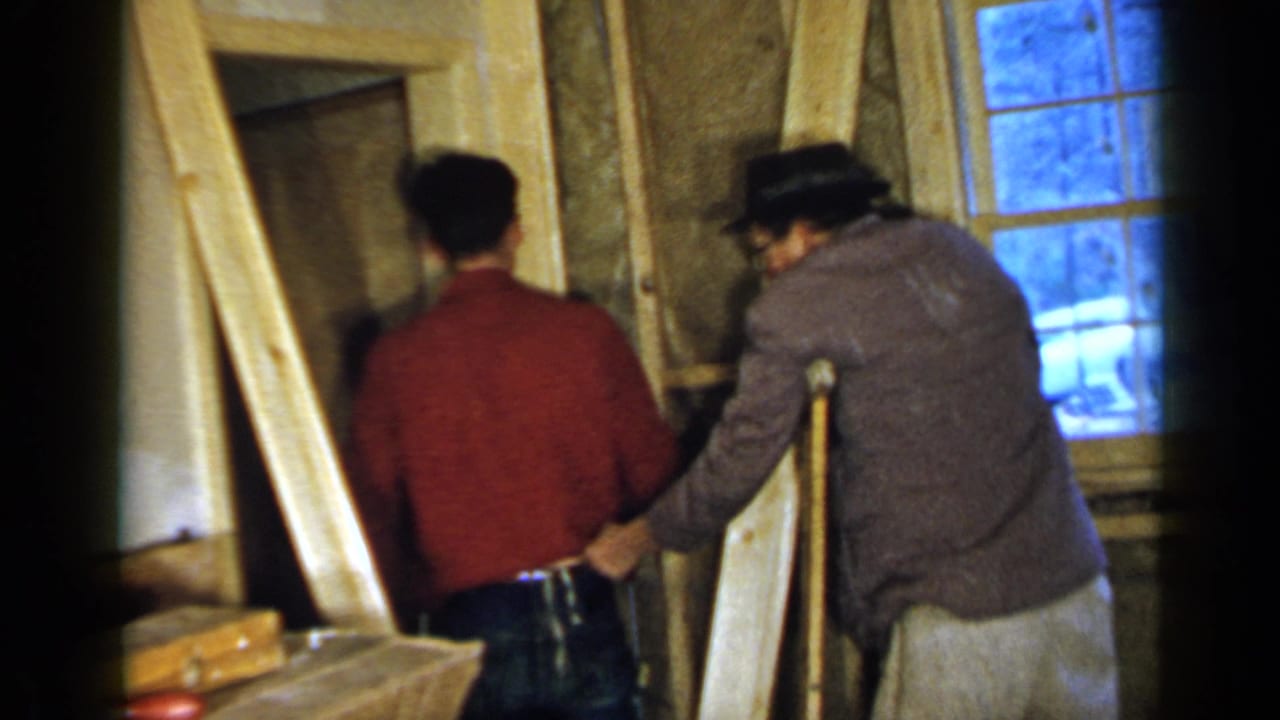 Two men stand by an unfinished doorway inside a framed room.