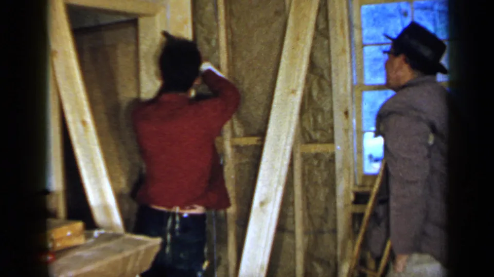 1957 Birmingham frame of a man hammering high on an unfinished wall while another man watches from beside the exposed framing and window.