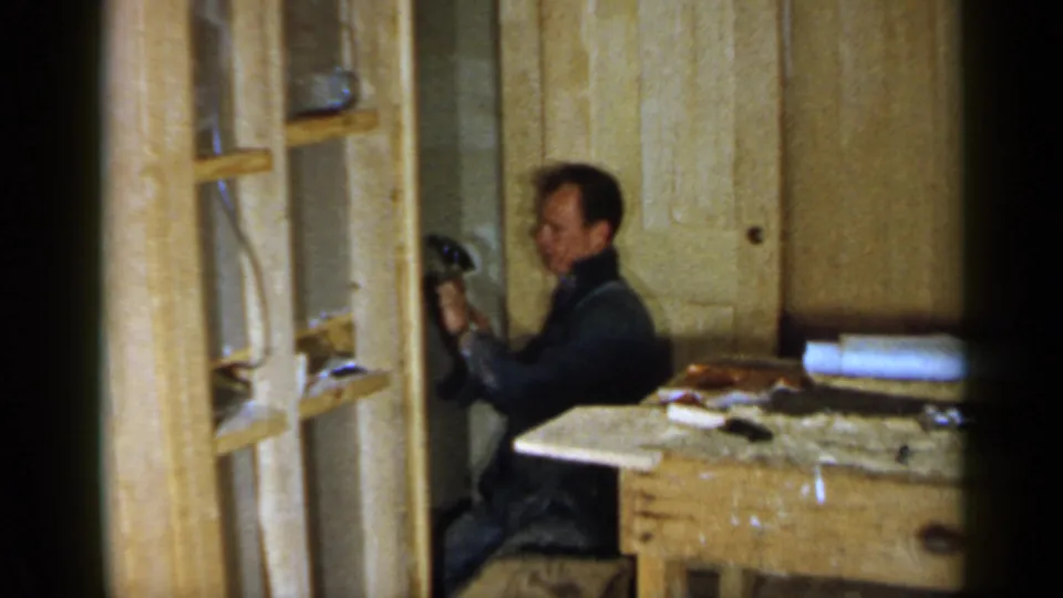 The man pauses or turns while working with a hammer in a wood-paneled 1957 Birmingham interior.