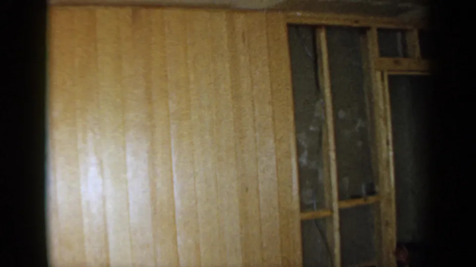 The final frame shifts away from the worker to wood paneling and a partially framed opening in the private interior.