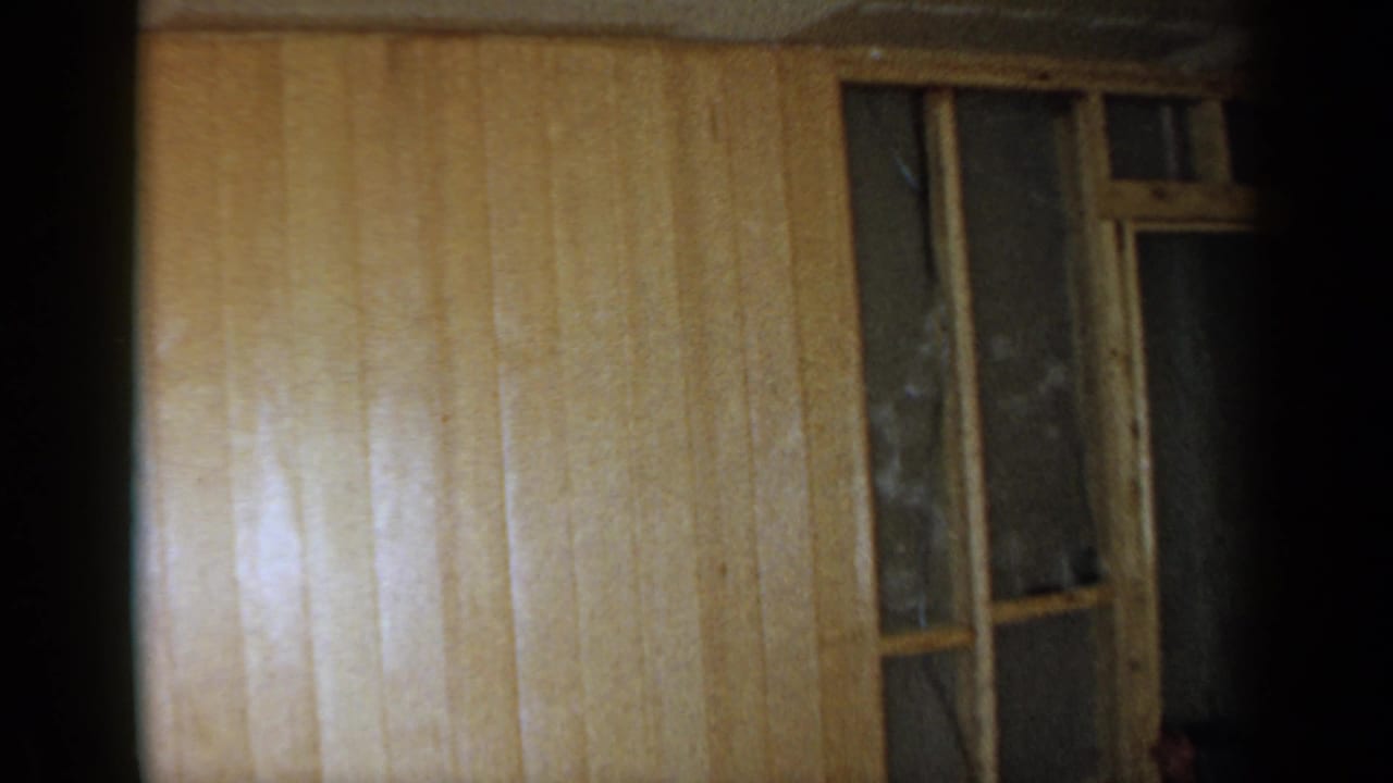 Wood-paneled interior wall with a tall window frame beside a dark unfinished area.