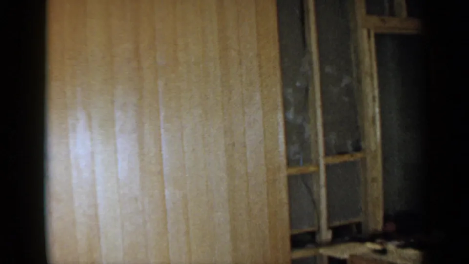 1957 Birmingham interior renovation view with pale paneling, a window frame, exposed dark wall area, and part of a wooden workbench at the edge.