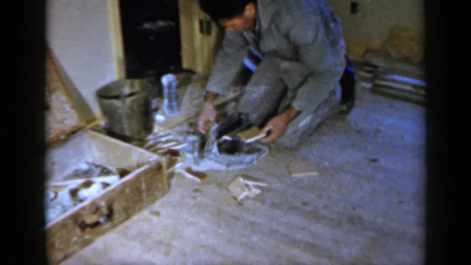 A man in gray work clothing works close to a circular floor opening in a private Birmingham interior, with tools and debris nearby.