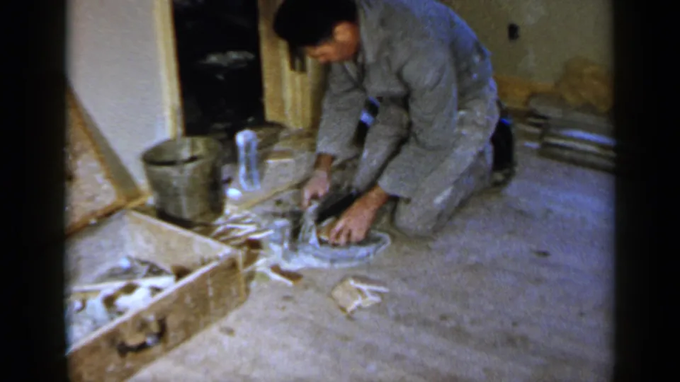 A man kneels in a private Birmingham interior, pressing or arranging material at a floor opening during home renovation work.