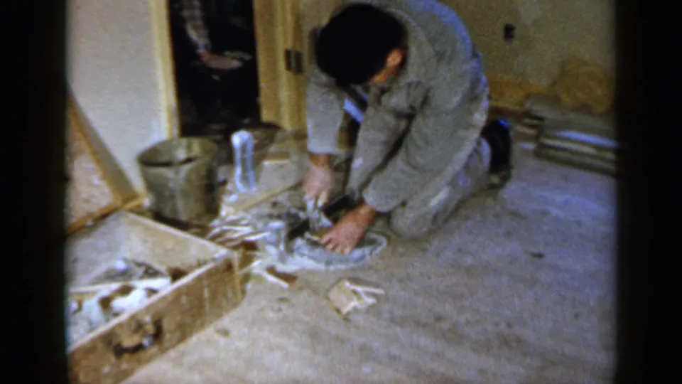 The man remains focused on a small construction task in a Birmingham interior, with tools or material near his hands.