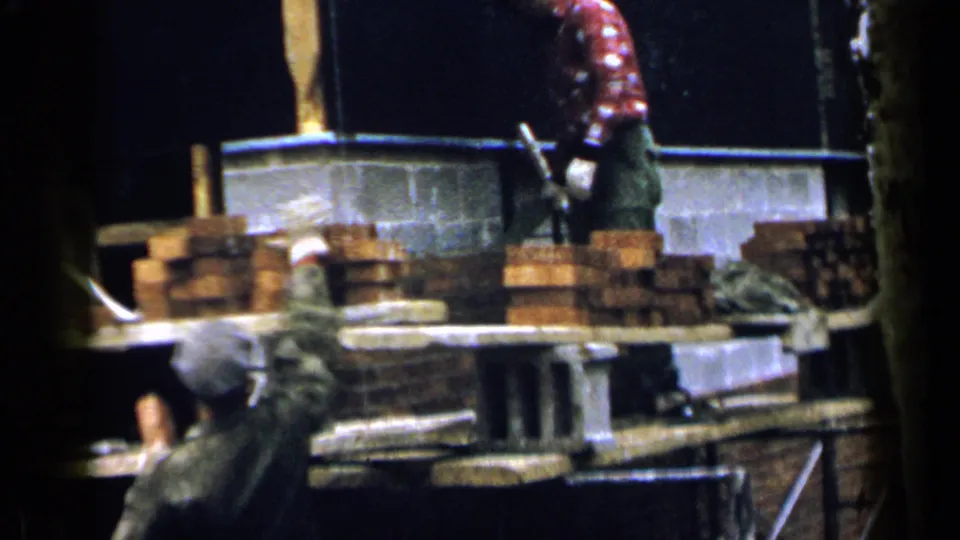 1957 Birmingham masonry work with stacked bricks, concrete blocks, and a passing worker partly visible near the scaffold.