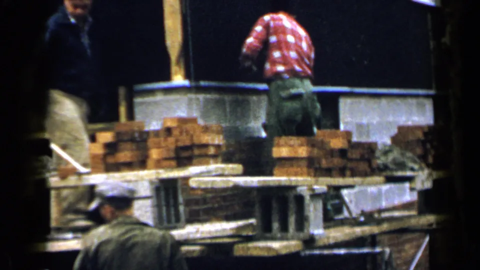 1957 Birmingham construction footage showing a bricklayer at a wall, stacked bricks, concrete blocks, and workers nearby.