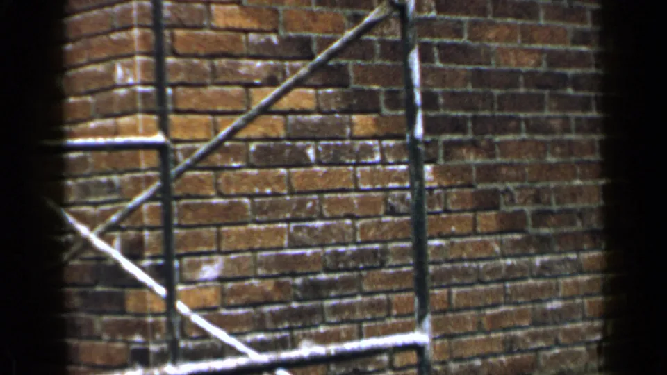 1957 Birmingham construction frame showing a newly laid brick wall section with metal railing or scaffolding crossing the view.