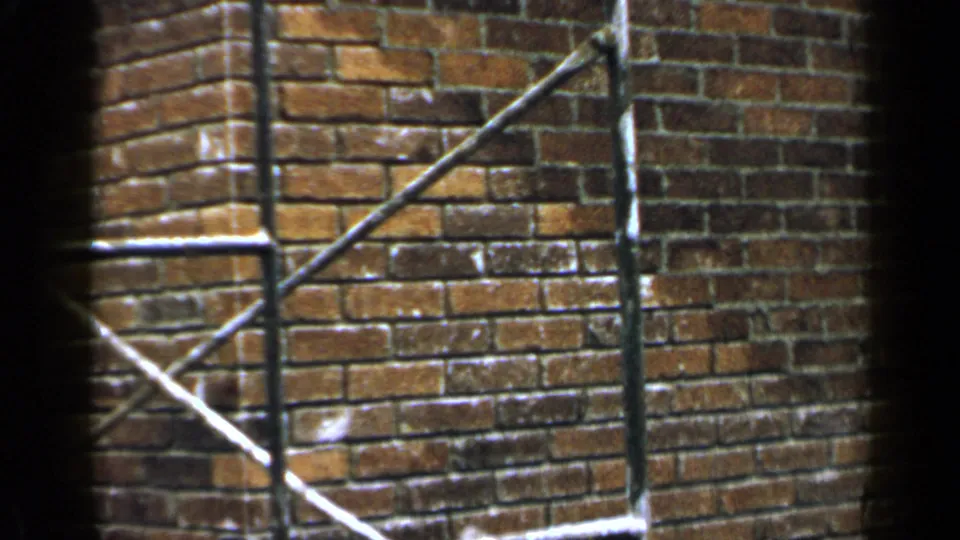 1957 Birmingham home-movie frame focused on brick masonry with metal rails or scaffolding in front of the wall.