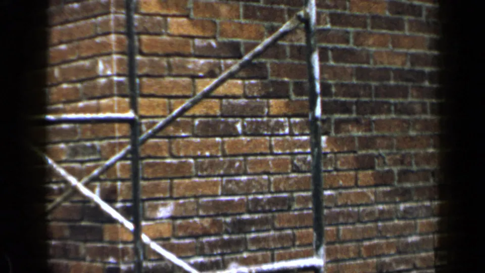1957 Birmingham home-movie frame showing a close brick wall corner with tubular scaffolding and diagonal braces.