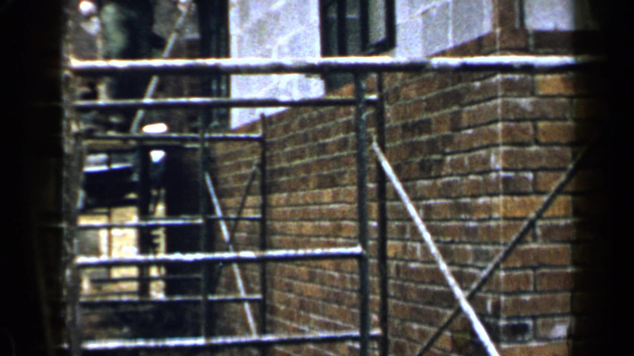 Metal scaffolding in front of brick and concrete building walls.