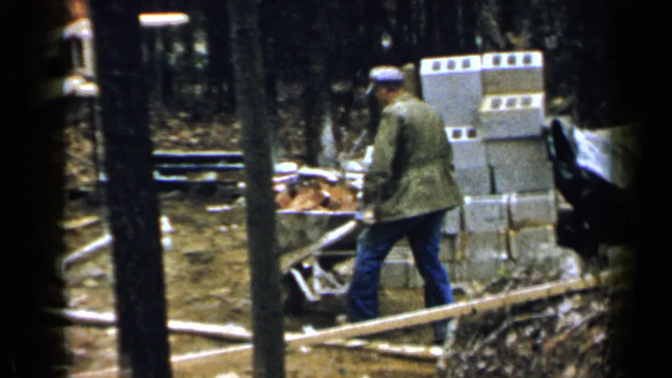 A man in a cap and work jacket walks near a wheelbarrow and stacked cinder blocks at the Birmingham construction site.