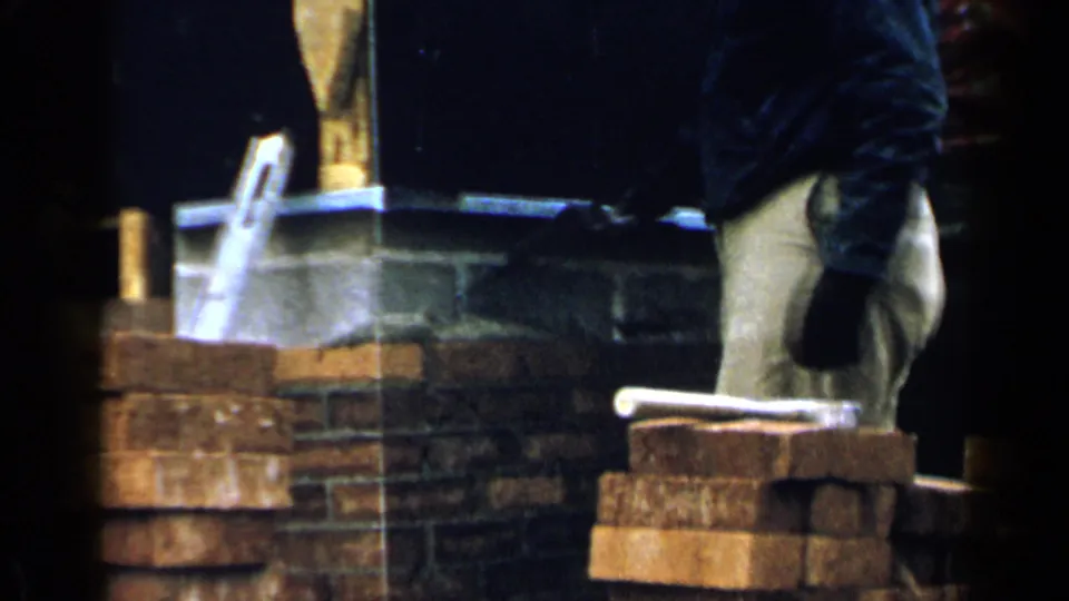 1957 Birmingham home-movie frame showing a gloved worker using a trowel around brick mortar work.