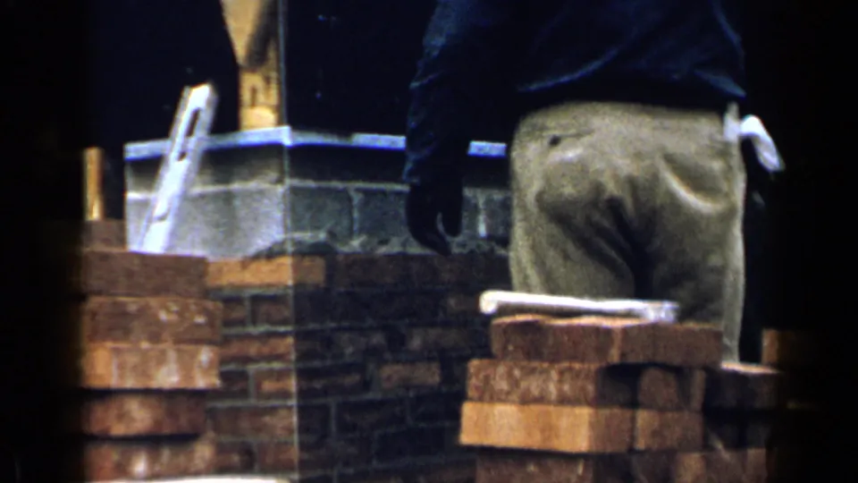 1957 Birmingham frame with the worker seen from behind beside a brick stack and partially built chimney.
