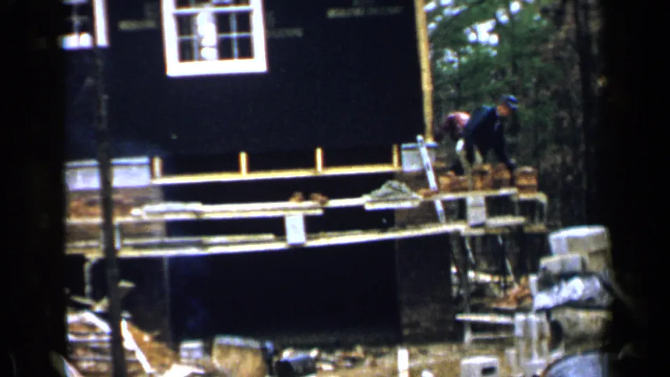 1957 Birmingham construction scene showing workers near a brick stack beside a partly framed residential wall.