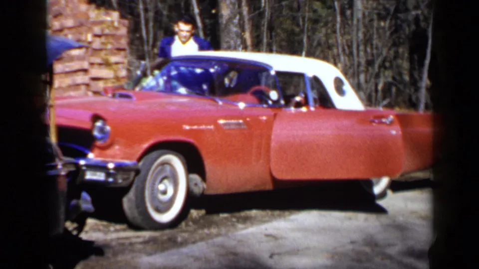 A red-and-white Ford Thunderbird appears parked near trees, with a man standing beside the open door in the 1957 Birmingham scene.
