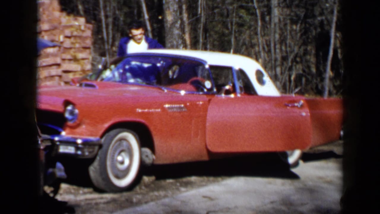 Red convertible with white roof parked on a driveway as a young man stands beside it.