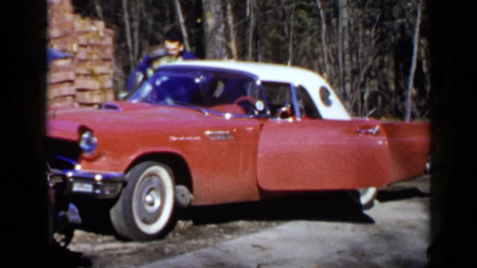 The red 1950s convertible remains parked in the driveway while a man in a blue jacket leans near the passenger area.