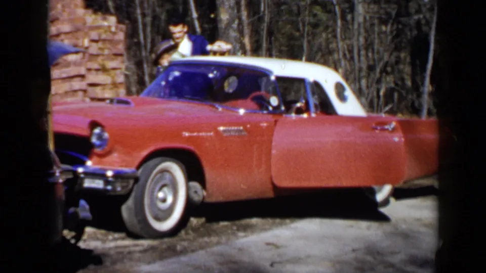 In the Birmingham 1957 home-movie frame, a young man appears to help an older man near the open red convertible.