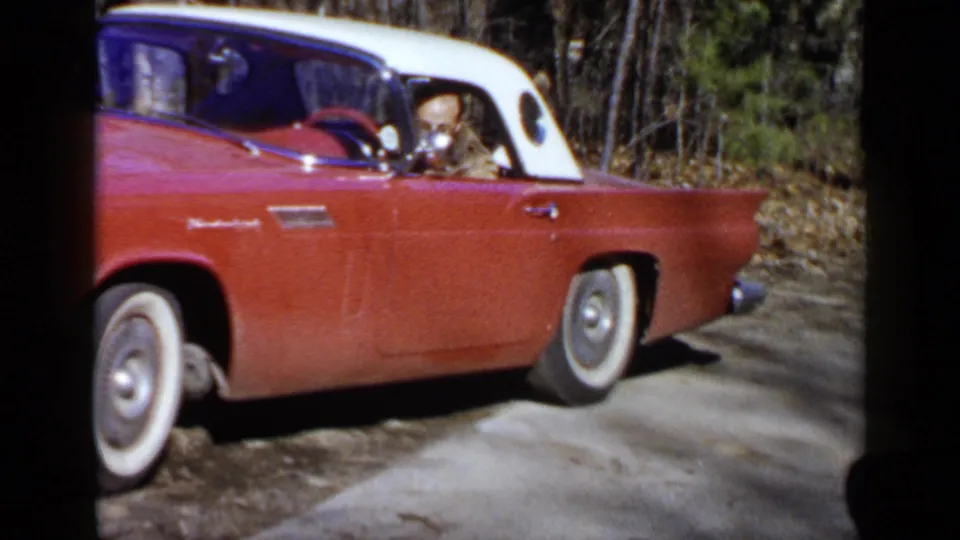 Side view of the red and white Thunderbird with a seated driver visible through the open window in Birmingham-area home-movie footage.
