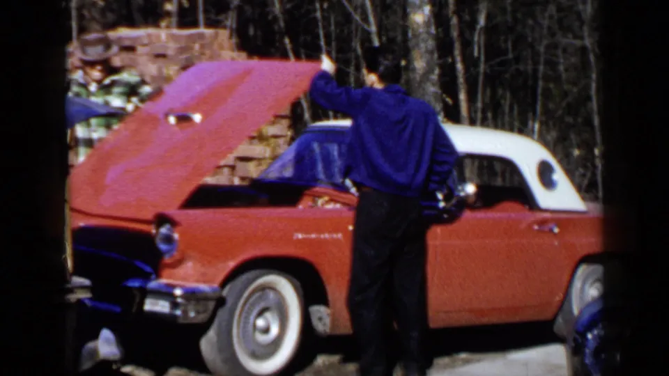 A man stands next to the red and white Thunderbird with the hood raised, while another person is partly visible near the front.