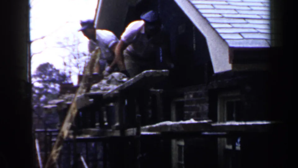 Two workers appear above a building exterior near a ladder or scaffolding in the 1957 Birmingham construction footage.