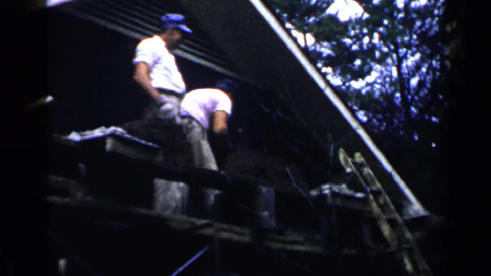 In 1957 Birmingham home-movie footage, two men appear to work on the roof of a large house amid trees.