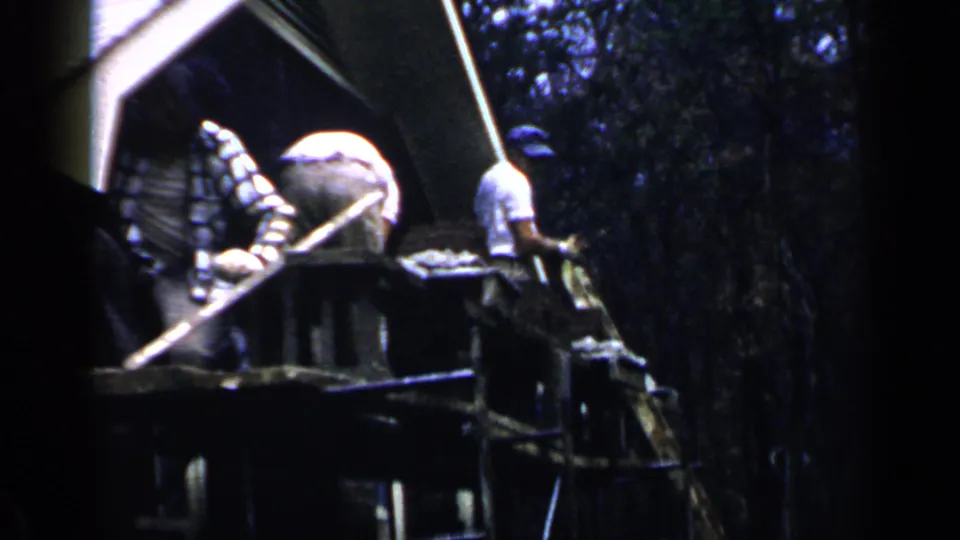 Workers on a Birmingham, Alabama construction scaffold in 1957, seen in soft 8mm color with trees behind them.