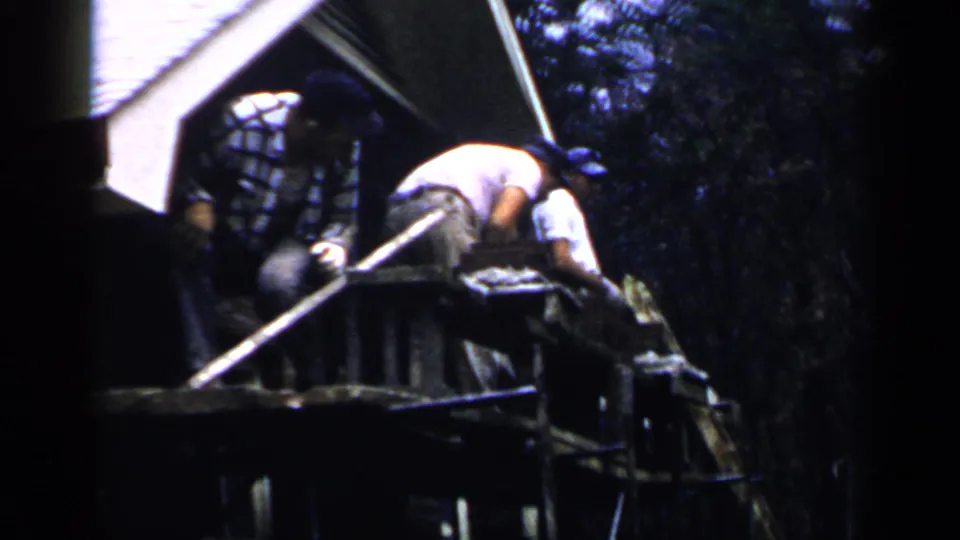 Close view of Birmingham construction workers on scaffolding, including a plaid-shirted man and a worker bent over the bricks.
