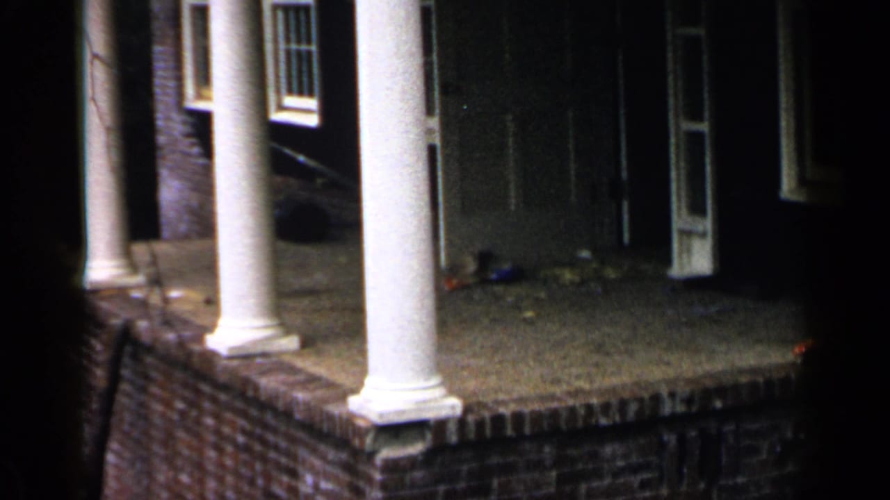 Brick porch with white columns, dark doorway, and windows at night.